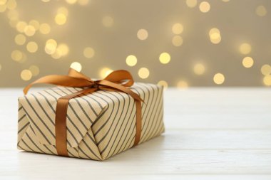 Bulanık ışıklara karşı beyaz ahşap masaya güzelce sarılmış bir hediye. Metin için boşluk