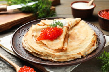 Kırmızı havyarlı lezzetli krepler, ekşi krema ve ahşap masada dereotu, yakın plan.