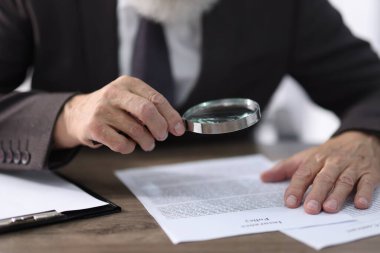 Ahşap masada belge okurken büyüteç kullanan kıdemli bir adam, yakın plan.