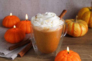 Cam bardakta kremalı balkabaklı latte, tarçın çubukları, taze sebzeler ve ahşap masada yanan mumlar, yakın plan.