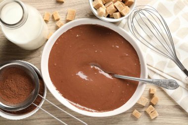 Kase içinde sıvı çikolata hamuru, kakao tozu, kahverengi şeker ve süt ahşap masada, düz yatıyordu.