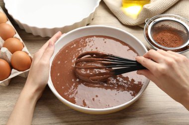 Kadın çikolatalı hamuru ahşap masada çırpıyla karıştırıyor.