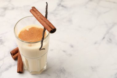 Bardakta lezzetli protein karışımı, beyaz mermer masada tarçın ve vanilya kapsülü, yakın plan. Metin için boşluk