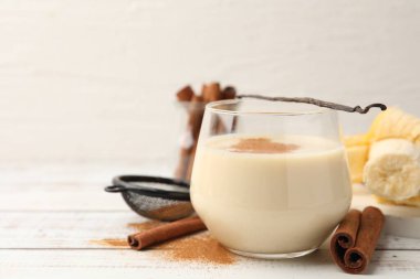 Bardakta lezzetli protein karışımı, tarçın, muz ve vanilya kapsülü beyaz ahşap masada, yakın plan. Metin için boşluk