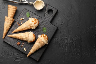 Lezzetli dondurma ve karamelli sos. Krep külahları siyah masada, düz yerde. Metin için boşluk