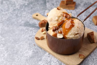 Karamel soslu lezzetli dondurma ve gri masada badem, yakın plan. Metin için boşluk