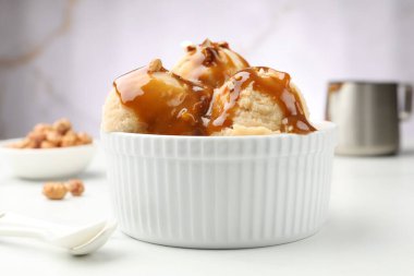Karamel soslu lezzetli dondurma ve beyaz masada badem, yakın plan.