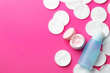 Pembe arka planda temiz pamuk pedleri ve kozmetik ürünleri, düz yatış. Metin için boşluk