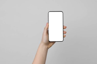 Açık gri arka planda boş ekranlı akıllı telefonu olan bir kadın, yakın plan. Tasarım için model