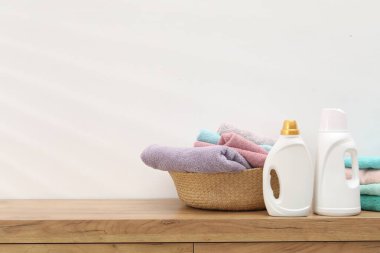 İçerideki beyaz duvarın yanındaki ahşap dolapta havlu ve şişe deterjan dolu çamaşır sepeti.