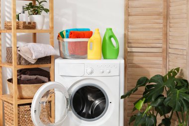 Çamaşır sepetinin içinde havlular ve çamaşır makinesinin üzerindeki deterjan şişeleri.