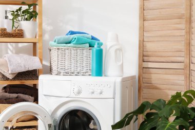 Çamaşır sepetinin içinde havlular ve çamaşır makinesinin üzerindeki deterjan şişeleri.