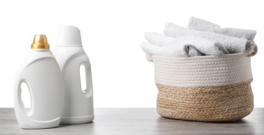 Çamaşır sepetinde havlular ve beyaz arka plandaki ahşap masada duran deterjan şişeleri.