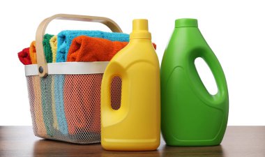 Çamaşır sepetinde havlular ve beyaz arka plandaki ahşap masada duran deterjan şişeleri.