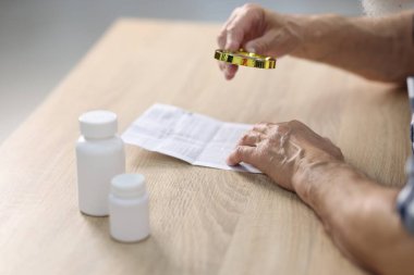 Ahşap masada tıbbi talimatları okurken büyüteç kullanan kıdemli adam, yakın plan.