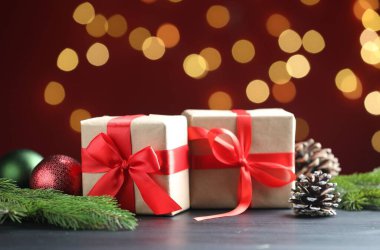 Paketlenmiş hediyeler ve Noel dekoru siyah masanın üzerinde kırmızı arka planda bokeh efektli, yakın plan. Metin için boşluk