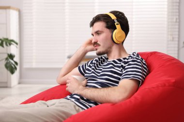 Kulaklıklı genç adam evde kahve poşeti koltukta müzik dinliyor.