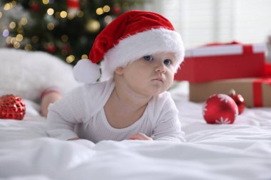 Noel Baba şapkalı şirin bir bebek ve evdeki yatakta takılar. Noel sezonu