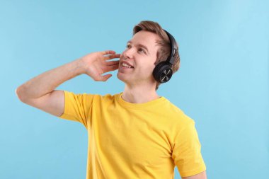 Kulaklıklı bir adam açık mavi arka planda müzik dinliyor.