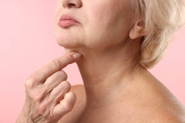 Üst düzey kadın açık pembe arka planda boynuna dokunuyor, yakın plan.