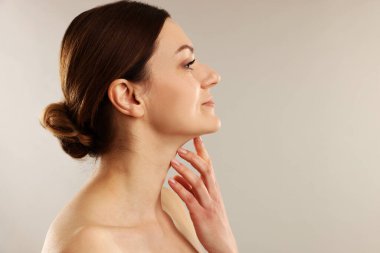 Açık gri arkaplanda boynuna dokunan kadın, metin için boşluk