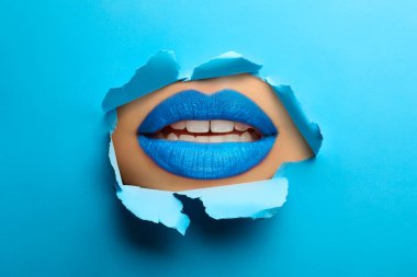 Güzel dolgun dudaklı kadın, mavi kağıttaki yırtık delikten bakıyor.