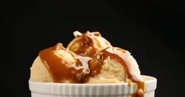 Karamel soslu lezzetli dondurma ve siyah arka planda badem, dönen. Yakın görünüm