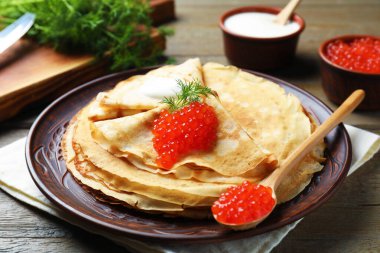 Kırmızı havyarlı lezzetli krepler, ekşi krema ve ahşap masada dereotu, yakın plan.