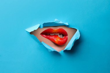 Güzel dolgun dudaklı kadın, mavi kağıttaki yırtık delikten bakıyor.
