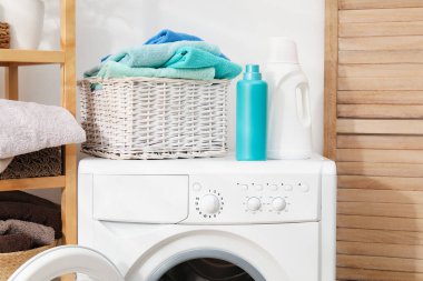 Çamaşır sepetinin içinde havlular ve çamaşır makinesinin üzerindeki deterjan şişeleri.