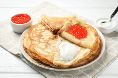 Kırmızı havyarlı leziz krepler ve beyaz ahşap masada ekşi krema, yakın plan.