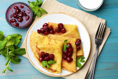 Açık mavi ahşap masada servis edilen kiraz reçelli leziz krepler.