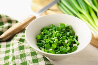 Beyaz ahşap masada yeşil soğanları kaseye koy, yakın plan.