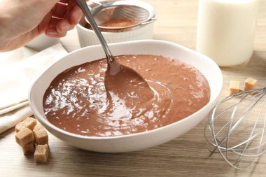 Ahşap masada kaşıkla çikolata hamuru alan kadın, yakın plan.