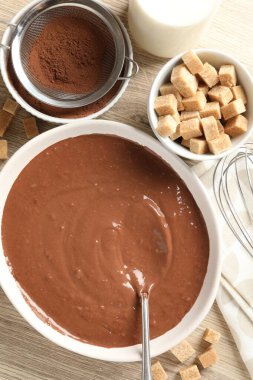 Kase içinde sıvı çikolata hamuru, kakao tozu, kahverengi şeker ve süt ahşap masada, düz yatıyordu.