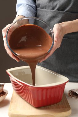 Kadın hafif ahşap masadaki yemek kabına çikolata hamuru döküyor, yakın plan.