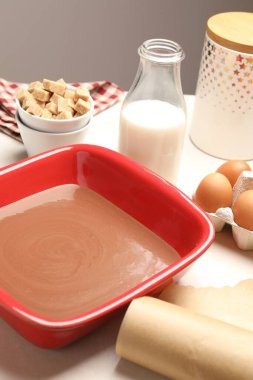 Sıvı çikolata hamuru fırın kabında, yumurta, kahverengi şeker ve süt beyaz masada, yakın plan.