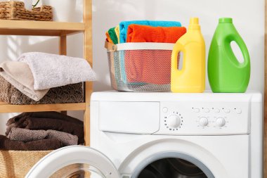 Çamaşır sepetinin içinde havlular ve çamaşır makinesinin üzerindeki deterjan şişeleri.