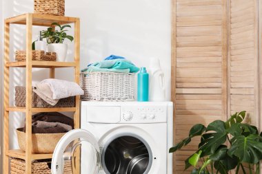 Çamaşır sepetinin içinde havlular ve çamaşır makinesinin üzerindeki deterjan şişeleri.