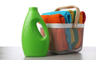 Çamaşır sepetinde havlular ve bir şişe deterjan beyaz arka plana karşı ahşap masada.