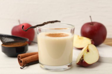 Bardakta lezzetli protein karışımı, tarçın, elma ve vanilya kapsülleri beyaz ahşap masada, yakın plan.