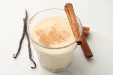 Bardakta lezzetli protein karışımı, beyaz masada tarçın ve vanilya kapsülleri, yakın plan.