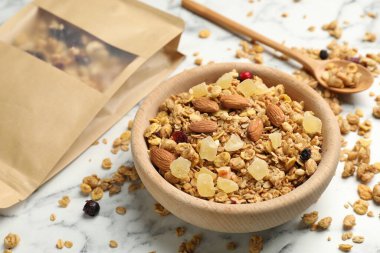 Lezzetli granola, kurutulmuş meyve ve fındıklar kasede ve kağıt torba beyaz mermer masada, yakın plan.