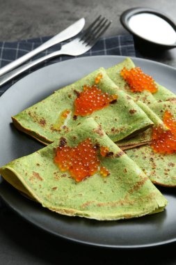 Kırmızı havyarlı lezzetli ıspanak krepleri ve gri masada ekşi krema, yakın plan.