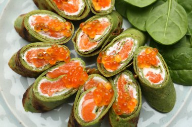 Somon, krem peynirli ıspanaklı krep, kırmızı havyar ve tabakta yapraklar.