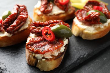 Krem peynirli lezzetli bruschettalar, güneşte kurutulmuş domatesler, kırmızı biber ve yeşil zeytinler masada, yakın plan.