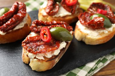 Krem peynirli lezzetli bruschettalar, güneşte kurutulmuş domatesler, kırmızı biber ve yeşil zeytinler masada, yakın plan.