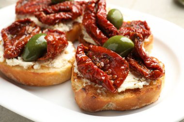 Krem peynirli lezzetli bruschettalar, güneşte kurutulmuş domatesler ve tabakta yeşil zeytinler, yakın plan.