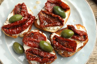 Krem peynirli nefis bruschettalar, güneşte kurutulmuş domatesler ve yeşil zeytinler masanın üstünde.