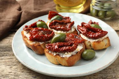 Krem peynirli lezzetli bruschettalar, güneşte kurutulmuş domatesler ve ahşap masada yeşil zeytinler, yakın plan.